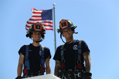Fire-personnel-standing-with-helmets-on-and-flag-in-background.jpg